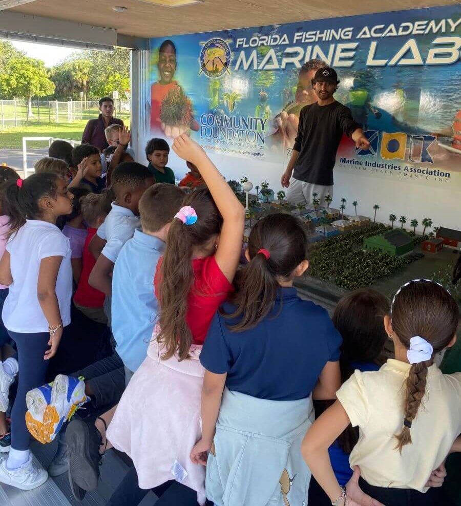 Students gather around the water and sand aquifer display in a class at Marine Lab. 